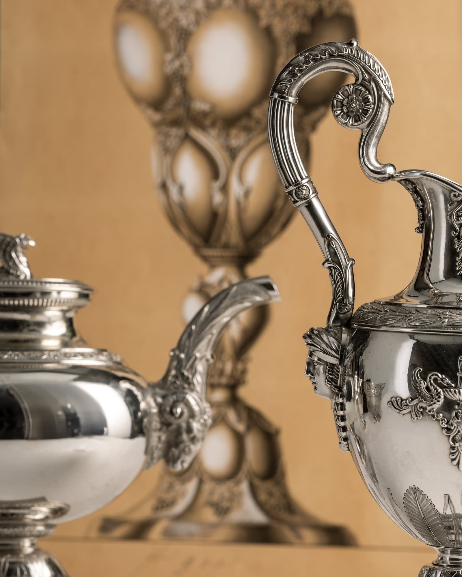 Kanne und Teekanne aus Silber, dahinter die Zeichnung eines Pokals