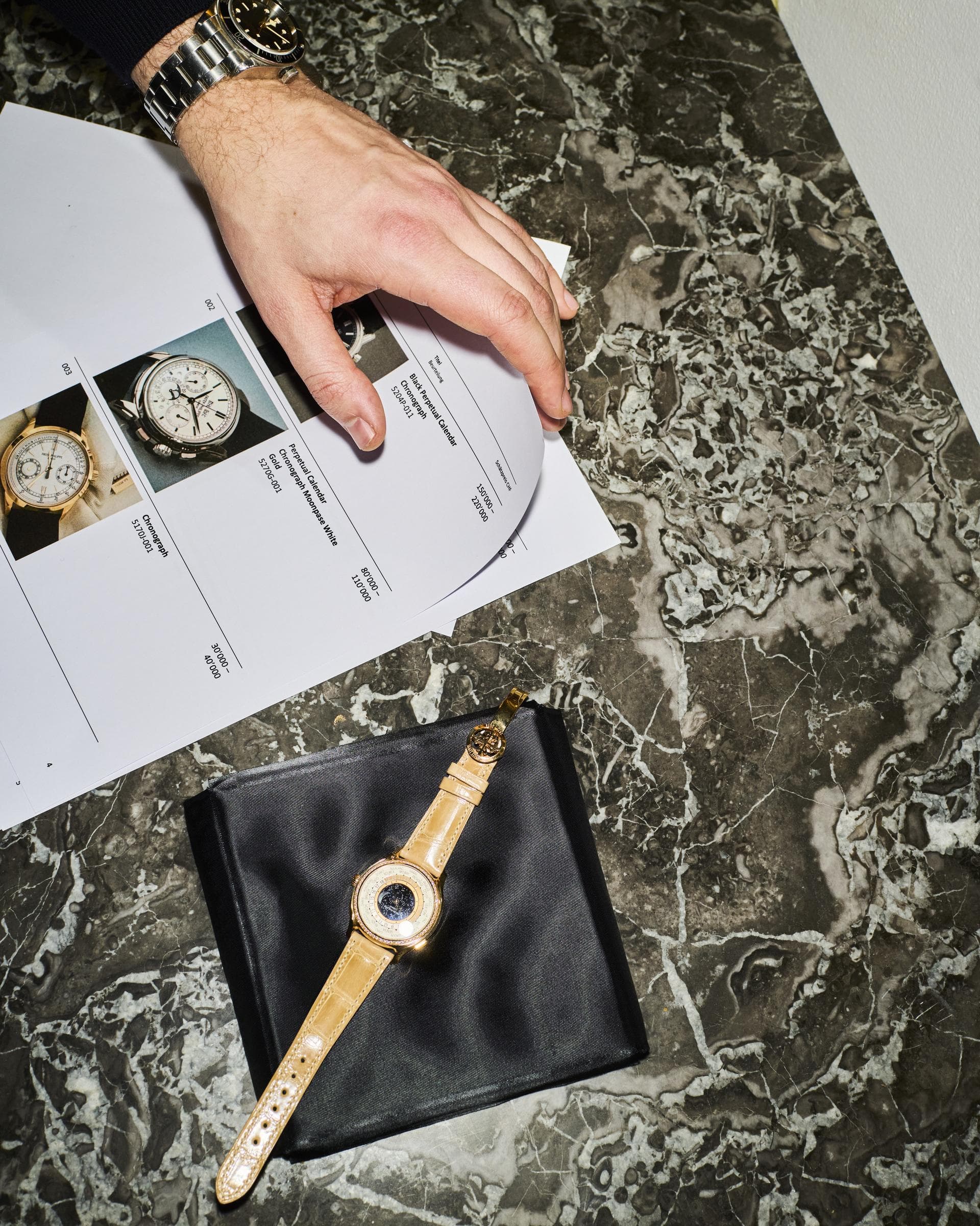 Hand auf einer Schätzungsliste für Armbanduhren, daneben eine Uhr auf Marmor