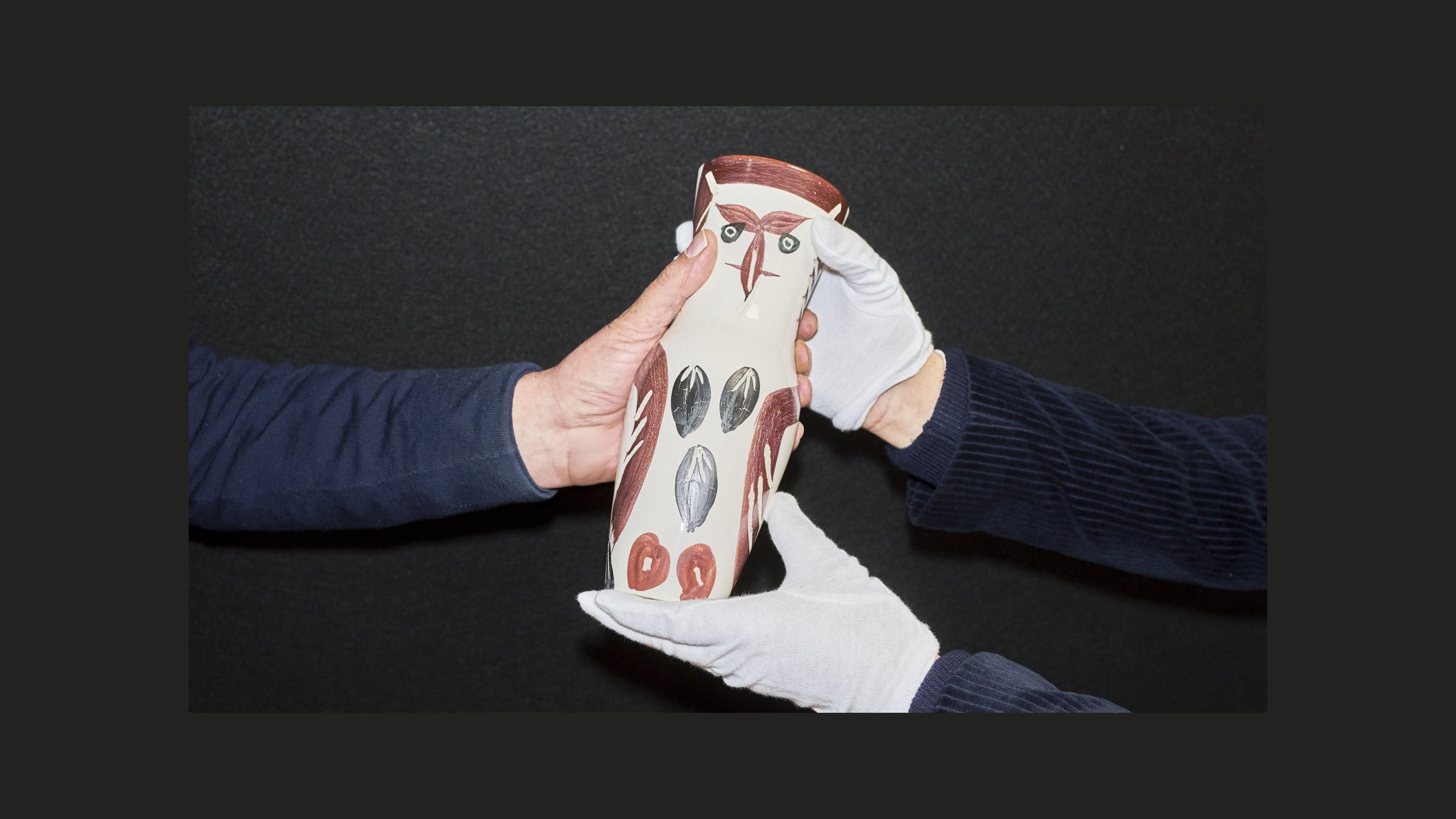 Übergabe einer Keramikvase mit Eulendekor von Hand zu Hand, mit weissen Handschuhen — Einliefern beim Auktionshaus Zofingen